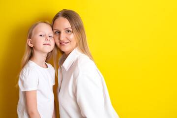 Cute beautiful mother and daughter in white clothes. Embrace the family. Yellow background place for text