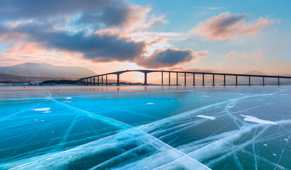 Arctic city of Tromso with Sandnessund bridge at sunset - Beautiful winter landscape with cracks on the surface of the blue ice in frozen lake - Tromso, Norway     