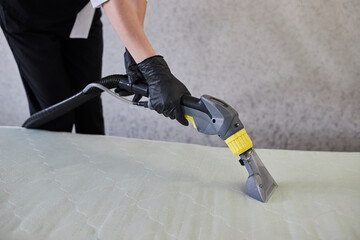 Cleaning service company employee removing dirt from furniture in flat with professional equipment. Female housekeeper arm cleaning the mattress on the bed with washing vacuum cleaner close up - 498700544