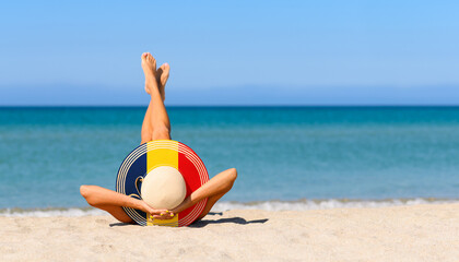 A slender girl on the beach in a straw hat in the colors of the flag of Romania. The concept of a perfect vacation in a resort in the Romania. Focus on the hat.