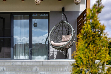 Modern hanging rattan chair with gray pillows on the summer garden terrace
