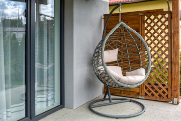 Modern hanging rattan chair with gray pillows on the summer garden terrace