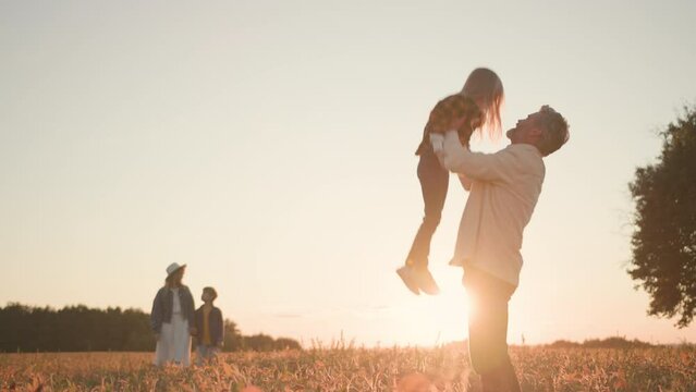 Family spending time together. Happy father throwing and catching his lovely daughter and having fun. Young mother walking with son outside sunny field.