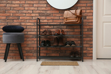 Rack with different shoes near red brick wall in hallway