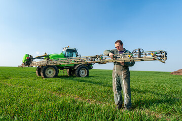 Epandage d'engrais liquide sur un champ de blé avec un épandeur automoteur. Agriculteur  ajustant le débit des buses - obrazy, fototapety, plakaty