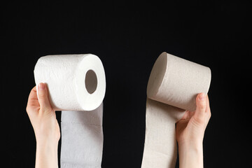 Two types of toilet paper in the hands of a person - white soft paper and gray from waste paper on a black background