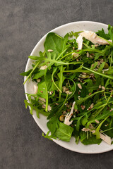 Delicious light salad with arugula and chicken breast sprinkled with various healthy seeds in a plate on a gray background, top view