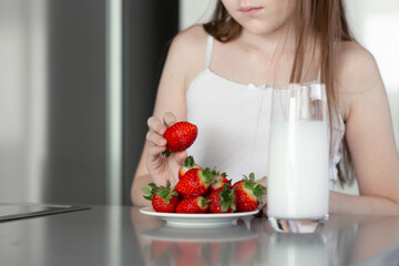 Preteen girl holding raw straberry, eating healthy food, drinking milk