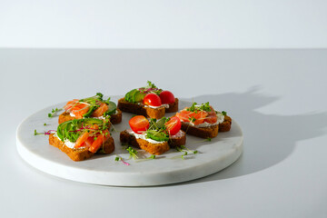 toasts with salmon, cottage cheese, avocado, microgreens, cherry tomatoes on white marble board on white background, open fish sandwiches