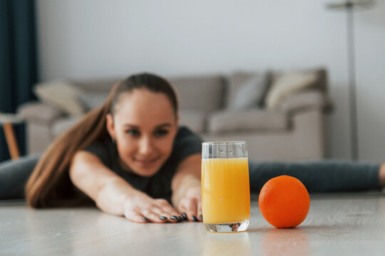 With orange fruit and juice. Young woman with slim body type and in yoga clothes is at home