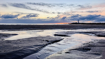 After sunset view of the lighthouse with wet sandy beach in the foreground