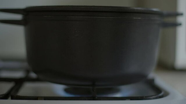Close-up putting cooking poton gas stove in kitchen at home. Unrecognizable Caucasian man cooking soup or porridge indoors. Blue gas burning under kitchen utensil