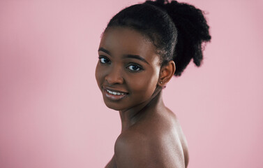 Looking in the camera. Portrait of young african american woman that is against pink background