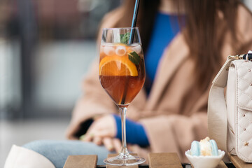 Young girl holding an aperol spritz. Aperol cocktail syringe in a glass. Young girl in a restaurant with a glass on a black background.