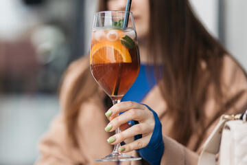 Young girl holding an aperol spritz. Aperol cocktail syringe in a glass. Young girl in a restaurant with a glass on a black background.