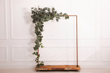 Stylish photo zone with wooden frame and green leaves indoors