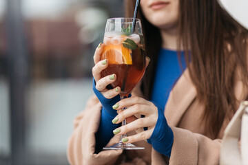Young girl holding an aperol spritz. Aperol cocktail syringe in a glass. Young girl in a restaurant with a glass on a black background.