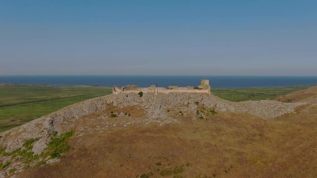 Drone tracking shot of Enisala, medieval fortress on top of a hill surrounded by lakes and plains on a clear sunny day