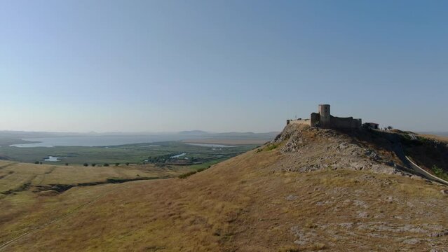 Aerial drone rising shot with front side of Enisala, medieval fortress on top of a hill surrounded by lakes and plains on a clear sunny day