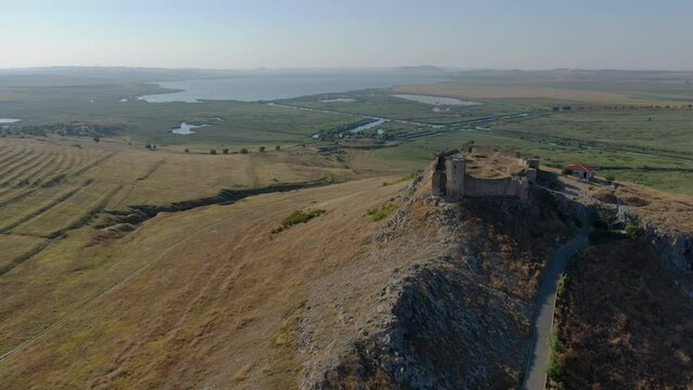 Drone tracking shot with front side of Enisala, medieval fortress on top of a hill surrounded by lakes and plains on a clear sunny day