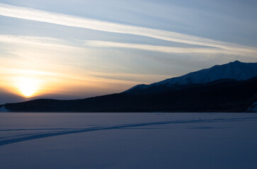 The last rays of the sun at sunset. The sun sets behind the mountains in the snowy desert.