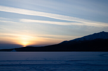 Fototapeta premium The last rays of the sun at sunset. The sun sets behind the mountains in the snowy desert.