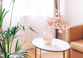 Soft home decor, glass jug, vase with white and pink beautiful flowers against window and curtains and table top. interior.
