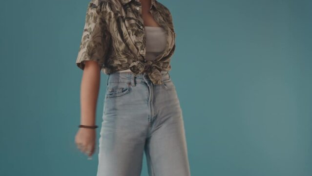 Tilt up slowmo of cheerful Asian teenage girl in stylish outfit and accessories making floss dance and laughing standing on turquoise background