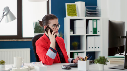 Business woman using smartphone to talk on phone call about financial growth in startup office. Marketing analyst with e commerce expertise having remote conversation on mobile phone.