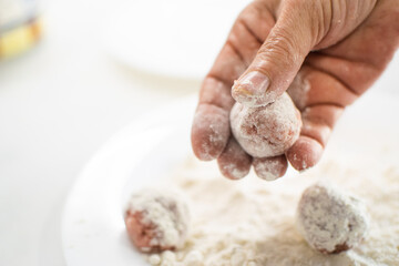 Hands making a meatball, kneading the meat with flour. Meatballs with flour on the background. Cooking, preparing. White, bright kitchen.