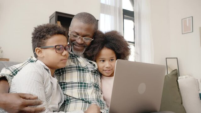 Smart african american little boy typing on laptop, grandfather embracing him and granddaughter, tracking shot
