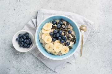 Healthy breakfast oatmeal porridge bowl with fruits and pumpkin seeds on grey concrete background. Top view