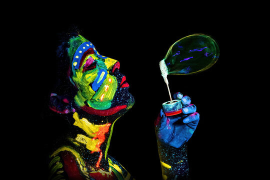Girl painted with UV colors blows a soap bubble