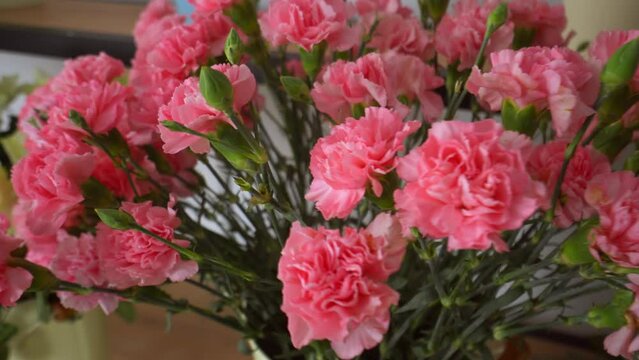 Close-up of a large number of pink carnations in a tin vase with handles on the background of other flowers on sale. The flowers are on display in a flower shop. Flower business.