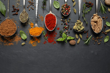 Different herbs and spices with spoons on black table, flat lay. Space for text