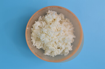 Cooked white rice in a plastic bowl isolated on a blue background