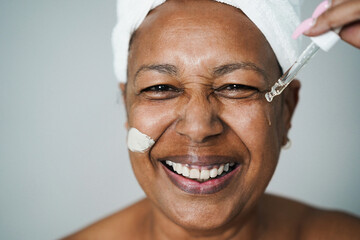 Senior african woman applying hyaluronic drop and skin mask beauty treatment on her face - Focus on...