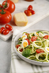 Keto paleo low-carb zoodles: zucchini noodles with parmesan cheese, cherry tomatoes, quail eggs on a checkered kitchen towel light grey surface