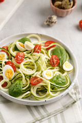 Keto paleo low-carb zoodles: zucchini noodles with parmesan cheese, cherry tomatoes, quail eggs on a checkered kitchen towel light grey surface