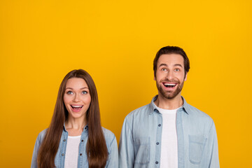 Photo of funny impressed husband wife wear jeans shirts looking up empty space isolated yellow color background
