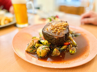 Beef steak with sauce, served on grilled vegetables and fried onions on a pub table with beer