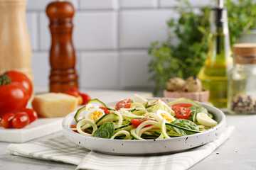 Keto paleo low-carb zoodles: zucchini noodles with parmesan cheese, cherry tomatoes, quail eggs on a checkered kitchen towel light grey surface
