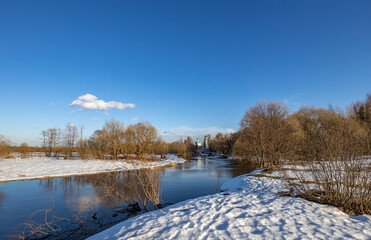 March sunny day by the river. A picturesque landscape, early spring, a river with snow-covered banks. The first thaws, the snow is melting.
