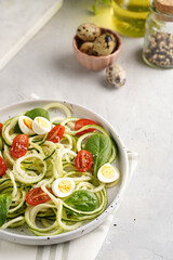 Keto paleo low-carb zoodles: zucchini noodles with parmesan cheese, cherry tomatoes, quail eggs on a checkered kitchen towel light grey surface