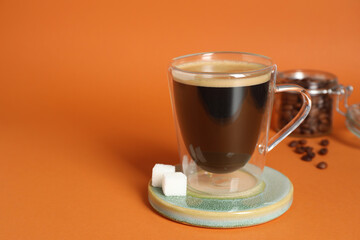 Coaster with cup of coffee on orange background, space for text