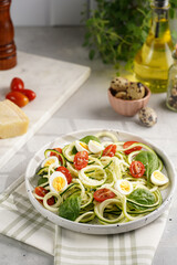 Keto paleo low-carb zoodles: zucchini noodles with parmesan cheese, cherry tomatoes, quail eggs on a checkered kitchen towel light grey surface