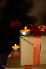 A burning candle on a Christmas present tied with a red ribbon. 
