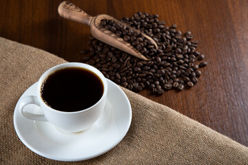 White cup of coffee with coffee beans on wooden background