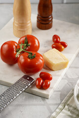 Ingredients for cooking: big tomatoes, small cherry tomatoes, parmesan cheese, oregano herb, salt and pepper mills on marble board
