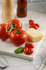 Ingredients for cooking: big tomatoes, small cherry tomatoes, parmesan cheese, oregano herb, salt and pepper mills on marble board